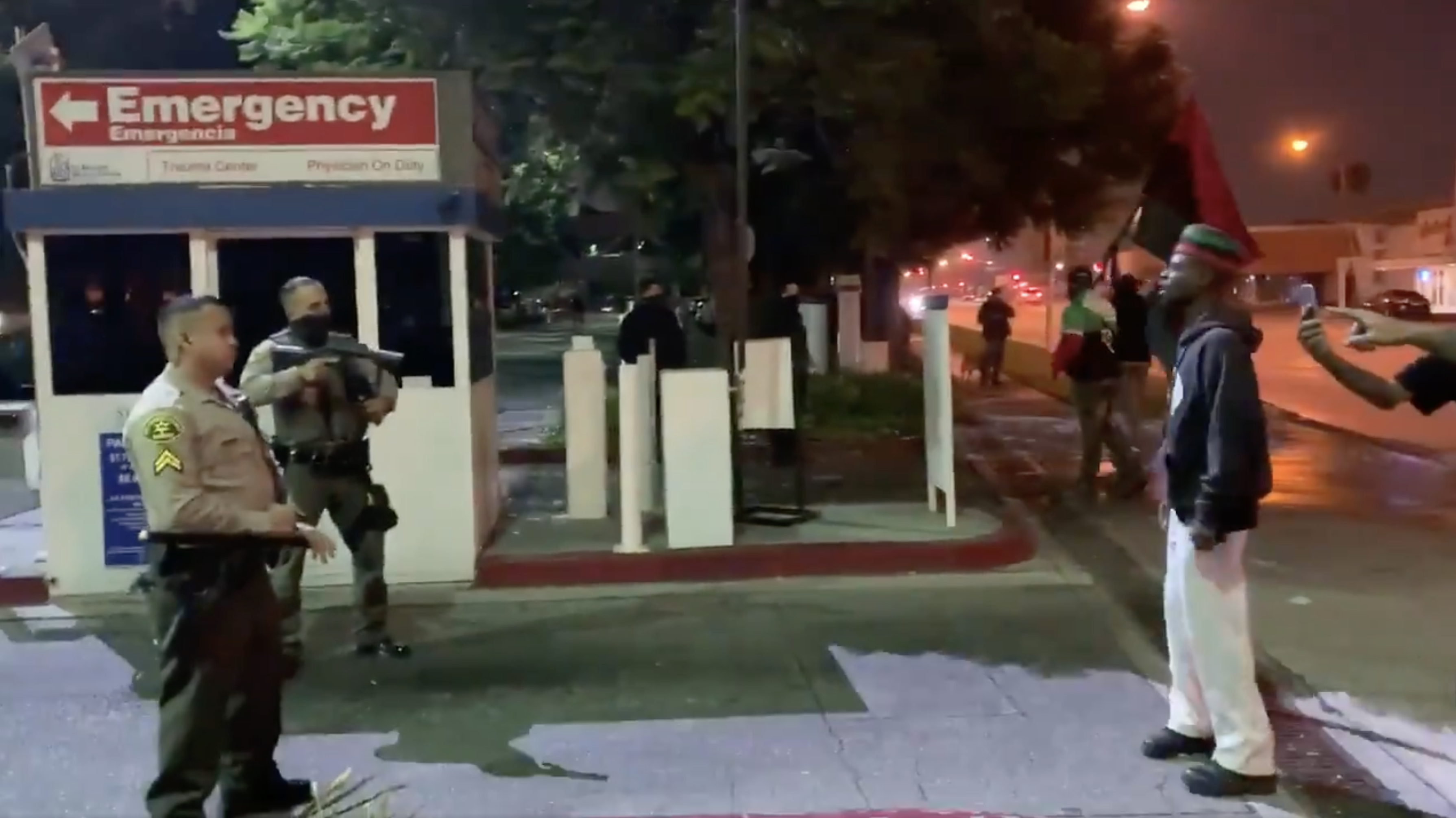 A small group of demonstrators outside a hospital in Lynwood, California confronted by Los Angeles Sheriff's Department deputies with their weapons aimed at them.